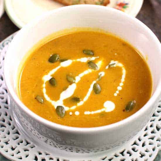 a bowl of pumpkin soup with cream and pumpkin seeds on top.