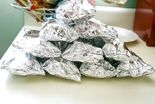 Stack of make-ahead freezer burritos wrapped in aluminum foil and ready for the freezer.