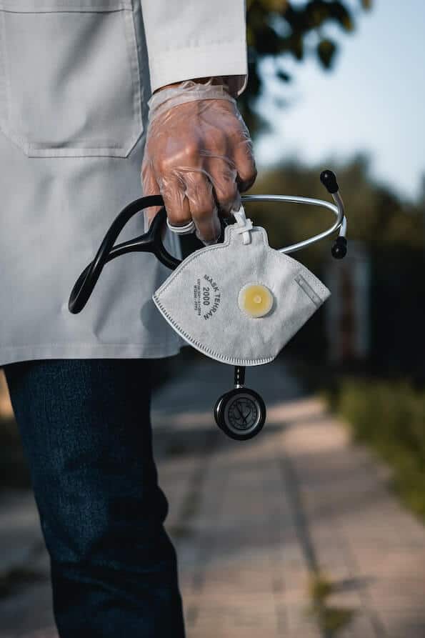 Doctor standing on walkway holding surgical mask and stethoscope in hand