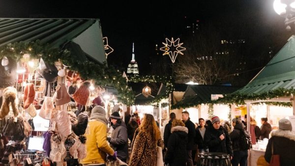The holiday market at nyc's union market at night with empire state building behind it.