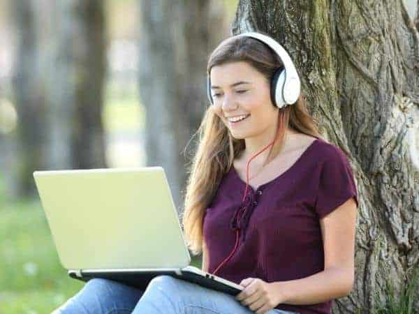 teen on a laptop sitting against a tree