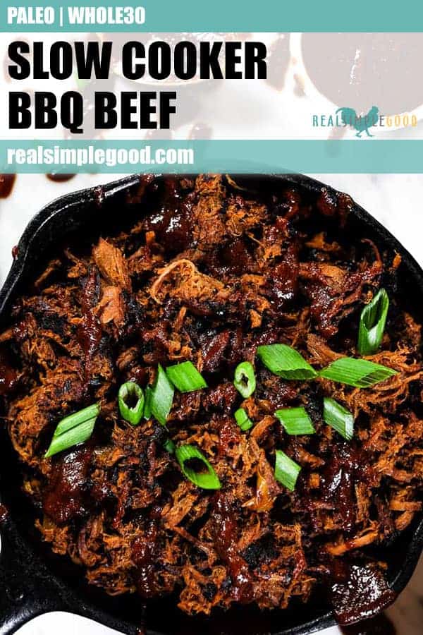 Slow cooker BBQ beef in a cast iron skillet, topped with extra BBQ sauce and chopped green onion.