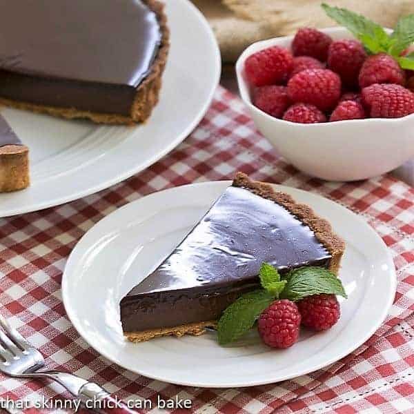 Ganache Topped Chocolate Tart - An almond crust with a silky, exquisite chocolate filling and topped with a rich ganache Ganache Topped Chocolate Tart on a white plate garnished with raspberries and mint
