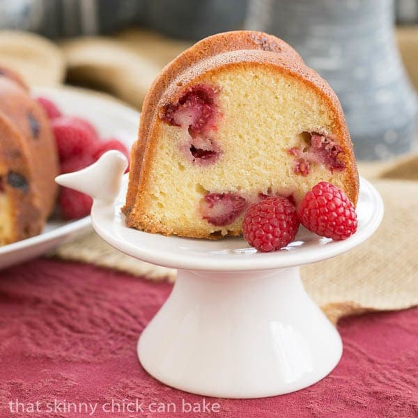 Raspberry Amaretto Bundt Cake - Pound cake full of fresh raspberries and flavored with extracts and liqueur Raspberry Amaretto Bundt Cake slice on a small white pedestal