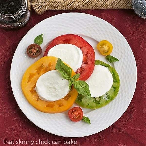 Salade de Tomates et Fromage - a simple French salad of juicy ripe tomatoes, fresh mozzarella and basil Overhead view Salade de Tomates et Fromage on a white basketweave plate