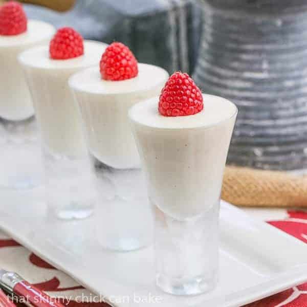 Vanilla Bean Cheesecake Shooters - Creamy, decadent, mini desserts! Vanilla Bean Cheesecake Shooters topped with raspberries on a white tray