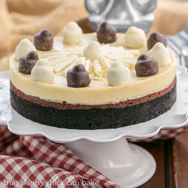 Layered Chocolate Cheesecake - A chocolate cookie crust topped with luscious dark chocolate and Frangelico white chocolate cheesecake. A delicious dessert for a holiday feast! Layered Chocolate Cheesecake on a white cake stand