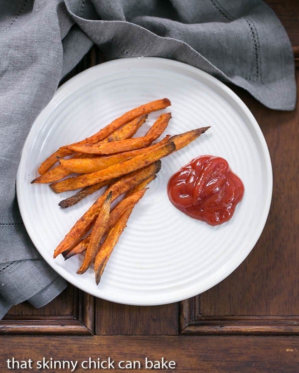 Spicy Sweet Potato Fries - Kicked up with paprika, cumin and cayenne pepper! Overhead view of Spicy Sweet Potato Fries on a white plate with ketchup