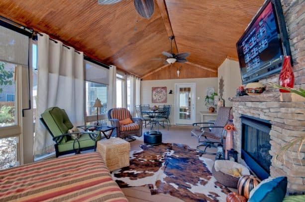 a southwestern screened porch with stone fireplace and white outdoor curtains