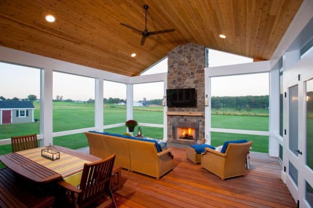 a stone fireplace in a simple, rustic screened porch