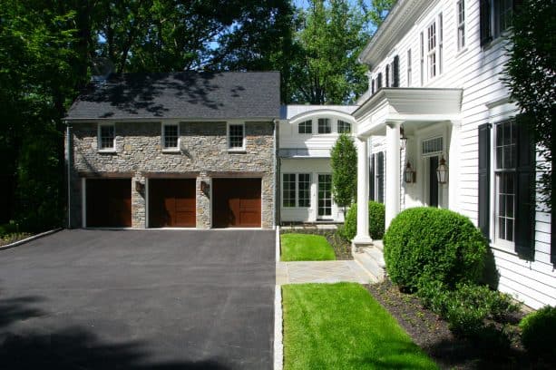 a stone garage located in front of a house with white siding material