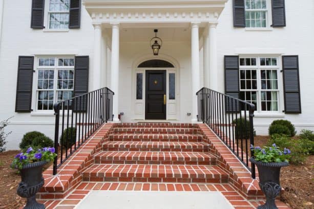 a traditional house with white-painted brick walls, black shutters, and red brick stairs