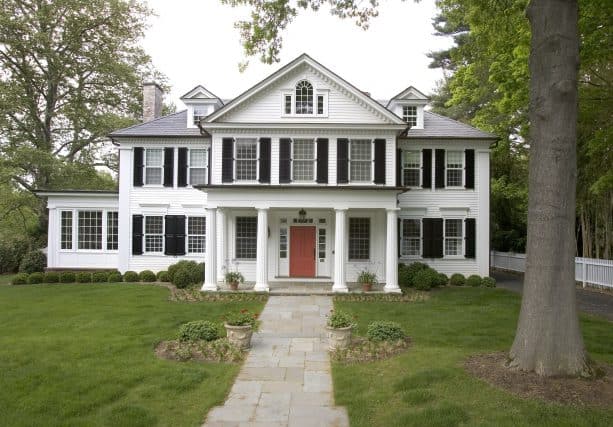 a white house with black shutters and coral red front door