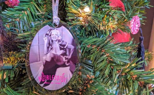 Close-up of ornament featuring b/w photo of Jennie Lee in Santa's helper outfit, hanging on a lit Christmas tree
