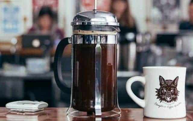 French press on a table next to a mug