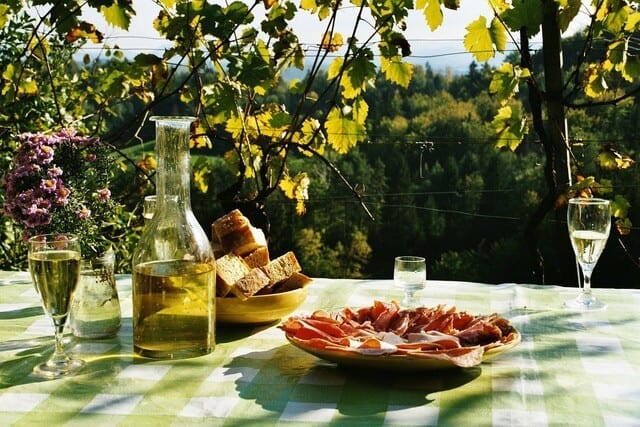a picnic table with a plate of meats and a carafe of wine.
