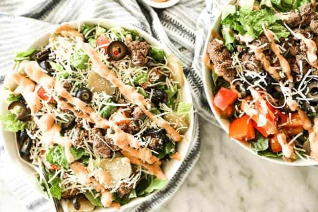 Two bowls of cheeseburger salad with shredded cheese on top and drizzled with special sauce.