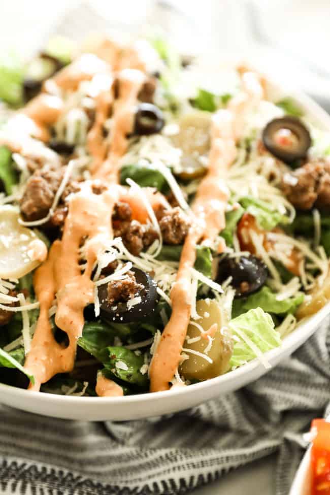 Close up angled image of cheeseburger salad in a bowl. Drizzle of special sauce over the top.