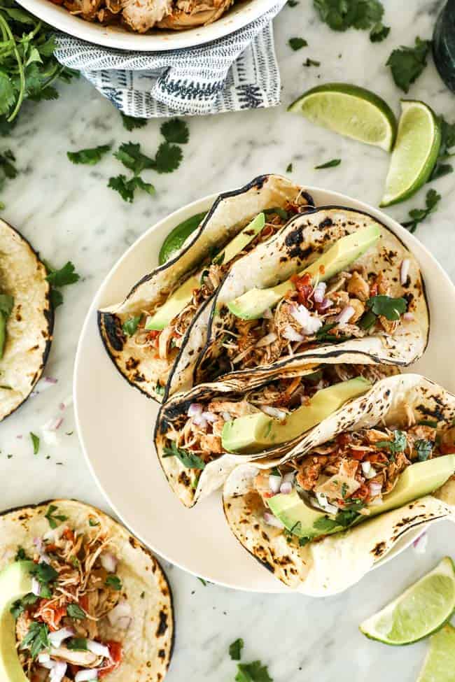Shredded chicken tacos on a plate. Toppings include avocado, red onion and cilantro.