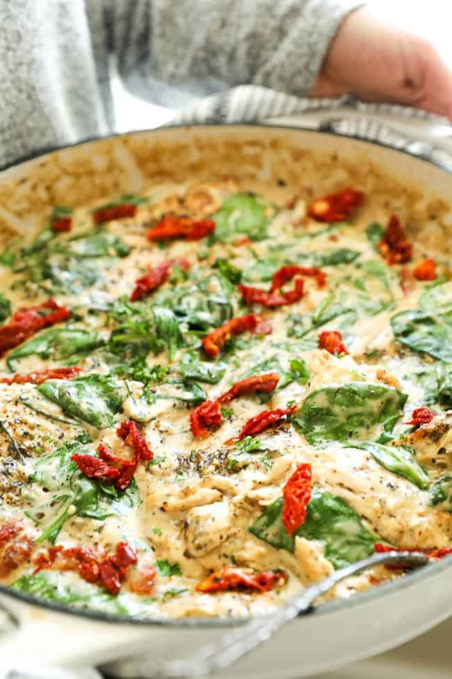Angled vertical image of holding skillet of creamy tuscan chicken with sun-dried tomatoes and fresh chopped parsley on top.