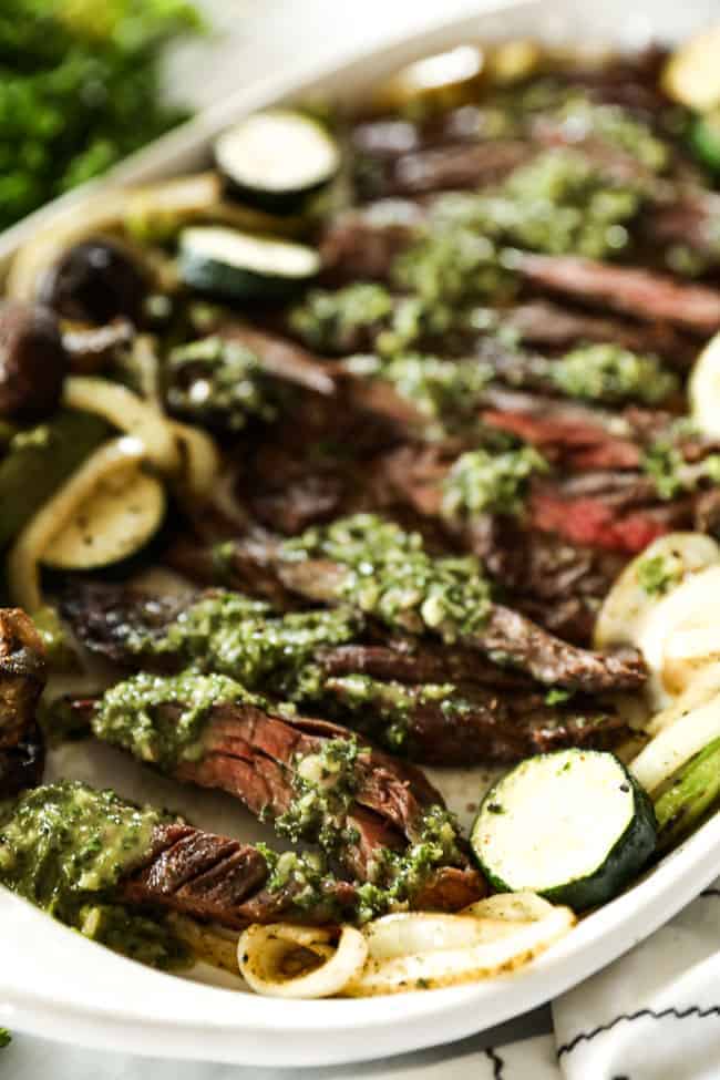 Close up of sauce drizzled all over chimichurri steak with grilled veggies on the side.
