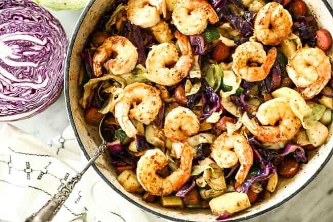 Shrimp and sausage skillet with cabbage, zucchini and mushrooms in a skillet with a serving spoon.