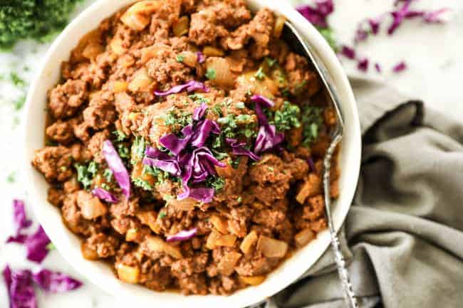 Horizontal image of instant pot sloppy joe's in a bowl with chopped parsley and purple cabbage on top. Serving spoon in bowl.