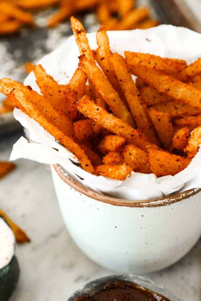 Vertical angled image of jicama fries in a mug with parchment paper.