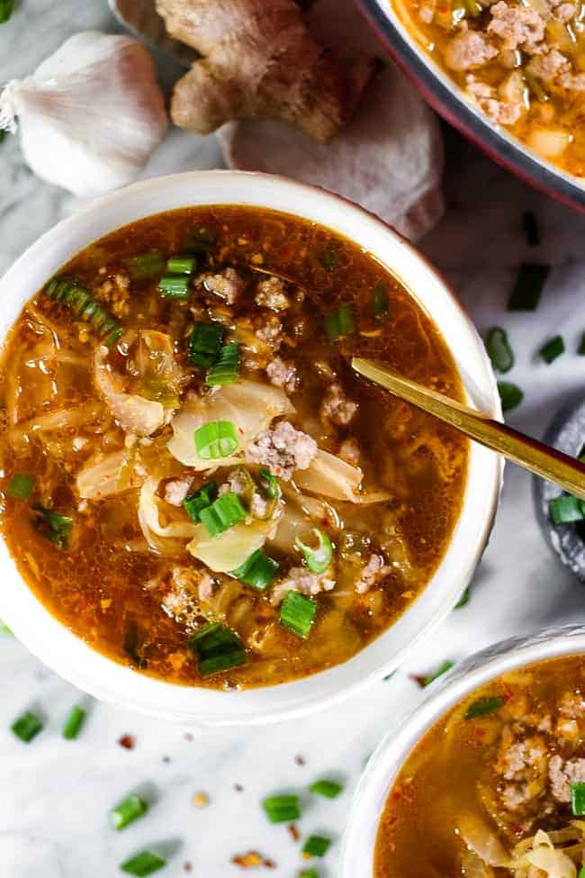 Bowl of kimchi soup with ground pork, topped with chopped green onion.