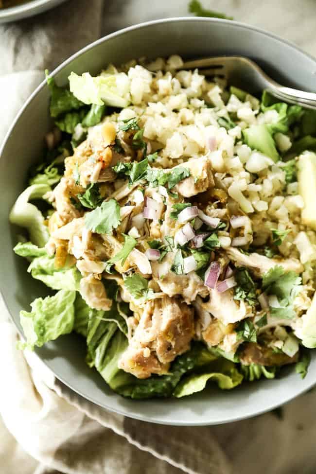 Close up of Mexican shredded chicken in a bowl with romaine lettuce, cauliflower rice and avocado. Topped chopped red onion and cilantro.