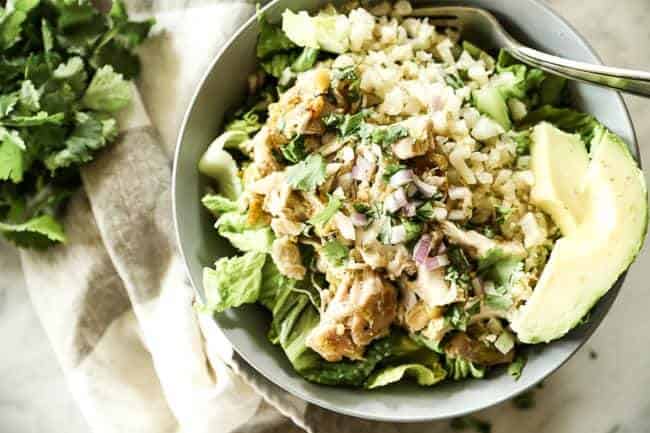 Mexican shredded chicken in a bowl with romaine lettuce, cauliflower rice and avocado. Topped chopped red onion and cilantro.