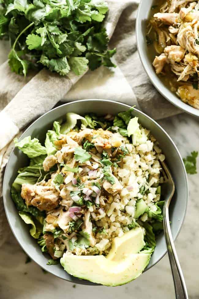 Mexican shredded chicken in a bowl with romaine lettuce, cauliflower rice and avocado. Topped chopped red onion and cilantro.