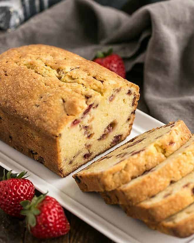 Fresh Strawberry Pound Cake - Dense, delicious, with sweet bits of fresh strawberries! Loaf of Fresh Strawberry Pound Cake on a white ceramic tray with half cut into slices