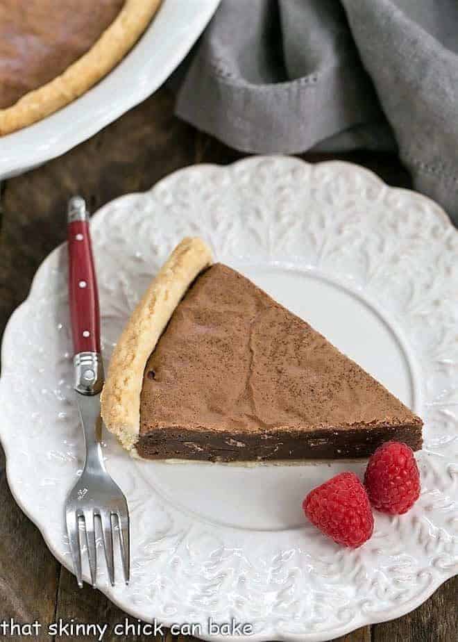 Fudgy Brownie Pie - Rich brownie filling studded with chocolate chips and baked in a flaky pastry shell! Fudgy Brownie Pie on a fancy white plate with raspberries and a red handled fork
