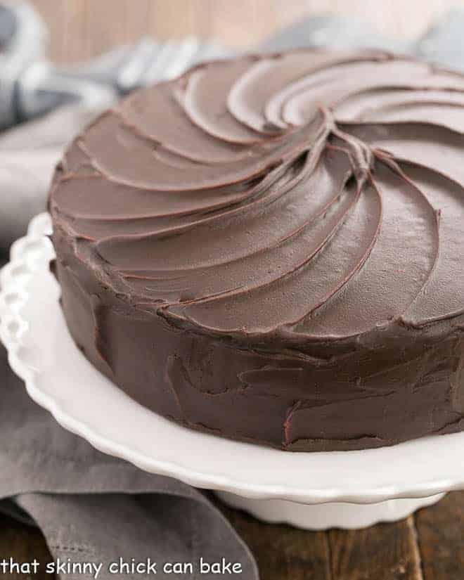 A rich, moist and tender 3-layer cocoa cake with a decadent, glossy chocolate ganache frosting! Perfect birthday or celebratory cake for your favorite chocoholic!! Triple Layer Cocoa Cake on a white cake ceramic stand