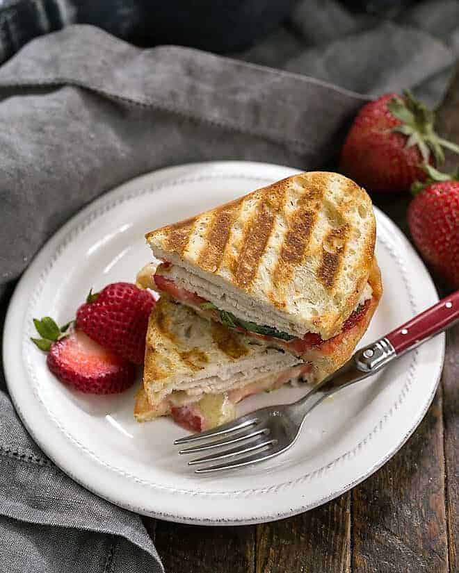 Strawberry, Turkey and Brie Grilled Cheese - an out of the ordinary grilled cheese with gooey Brie, sweet strawberries, spicy jelly and salty deli turkey! Strawberry, Turkey and Brie Grilled Cheese stacked on a white lunch plate with a red handled fork