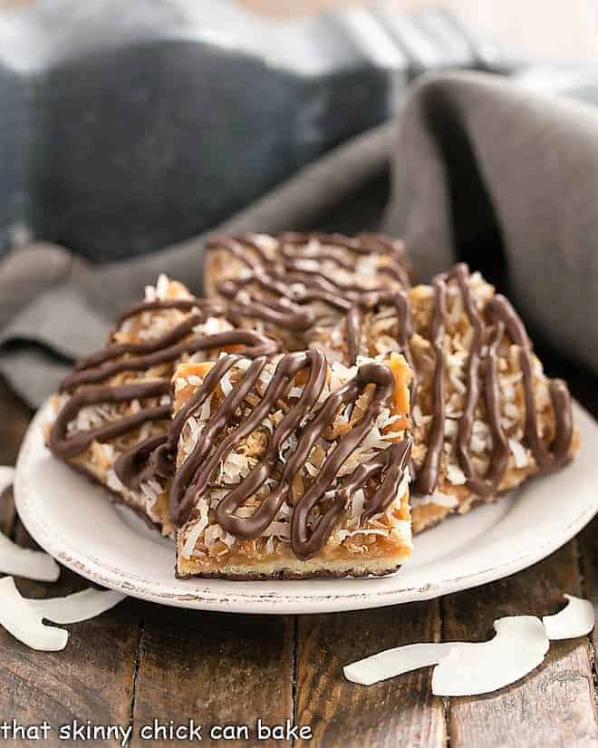 Homemade Samoa Bars - all the same terrific flavors of the classic Girl Scout Cookies with a shortbread base, caramel and coconut topping and chocolate drizzle! Homemade samoa bars on a round plate with shreds of coconut