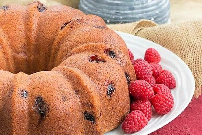 Raspberry Amaretto Bundt Cake on a cake plate with fresh raspberries