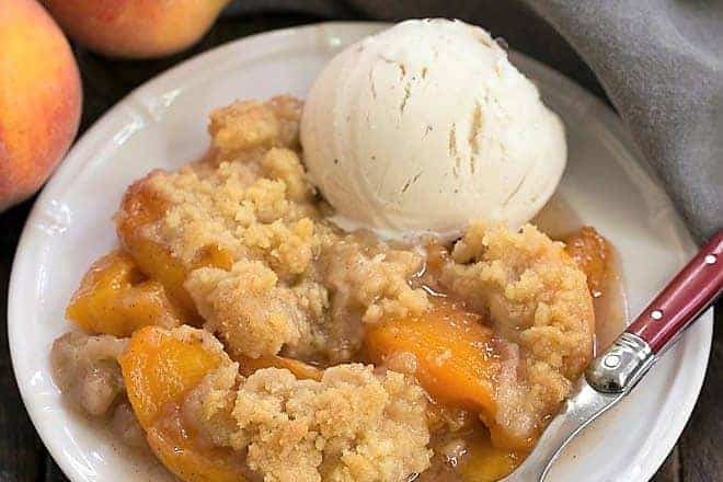 Classic Peach Crisp on a white plate with a scoop of vanilla ice cream