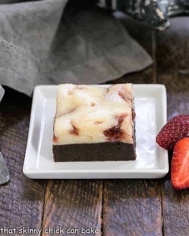 A rich fudgy brownie topped with cheesecake swirled with strawberry jam for a decadent dessert everyone will adore! A strawberry brownie on a square white plate with fresh strawberries