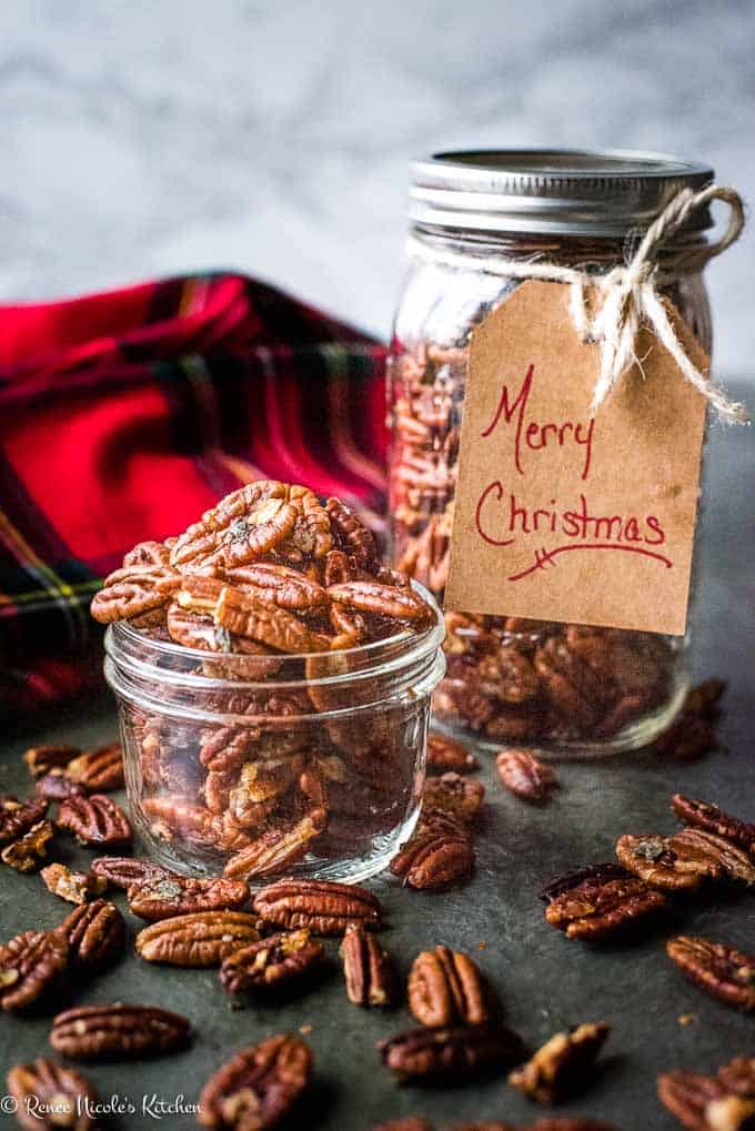 Brown Butter Roasted Pecans shown as a great DIY homemade gift. Pecans spilling out of a short glass jar in front of a tall glass jar of pecans with the tag "Merry Christmas" tied to it.