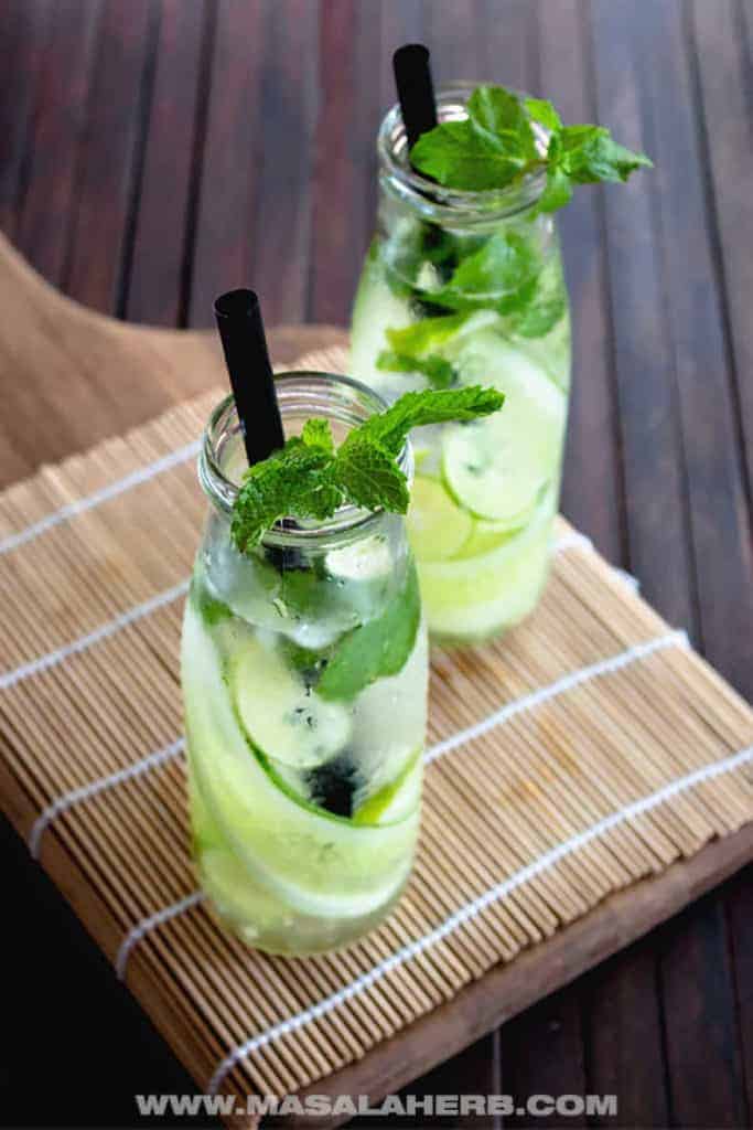 two glasses of cucumber mint water on a bamboo placemat on a wooden surface