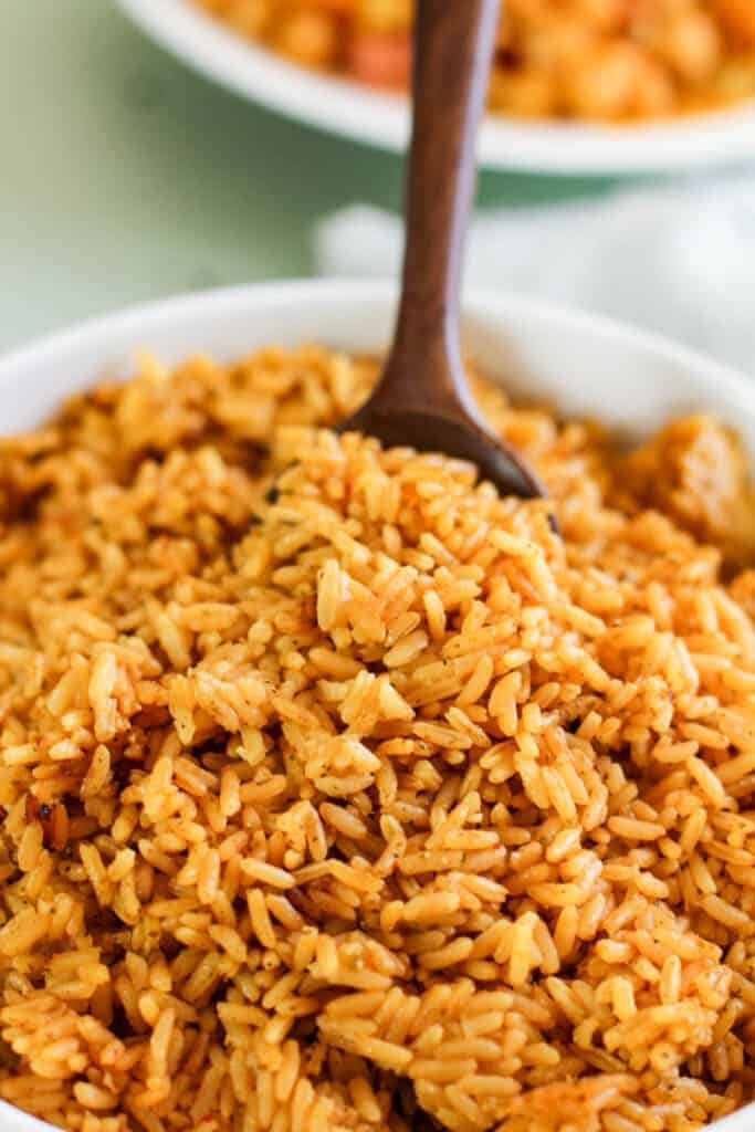 wooden spoon in the center of white bowl filled with yellow rice