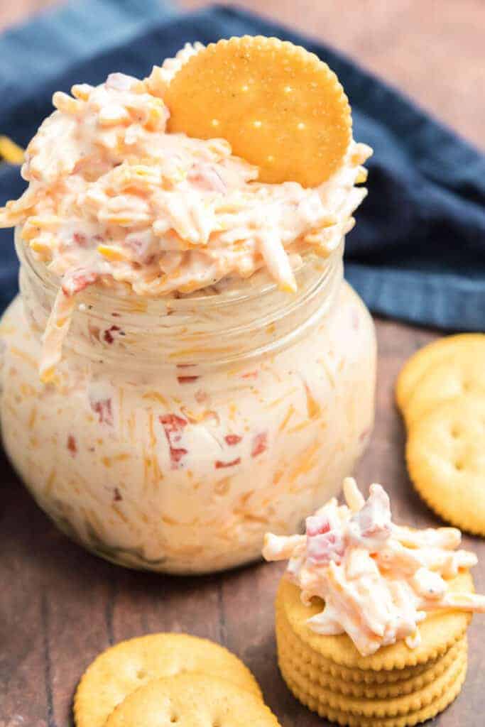 pimento cheese dip in a mason jar with a ritz cracker sticking out of the top