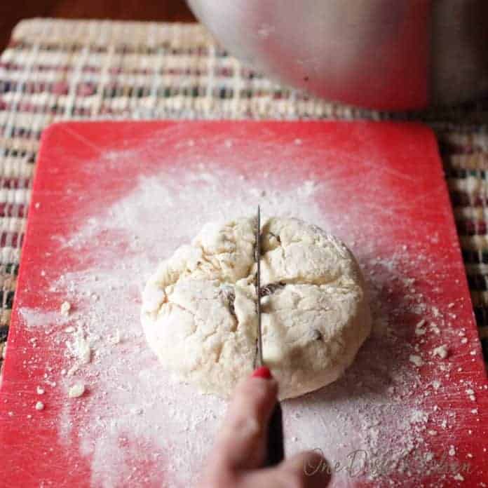 Scoring a cross with a knife into the dough of irish soda bread on a cutting board