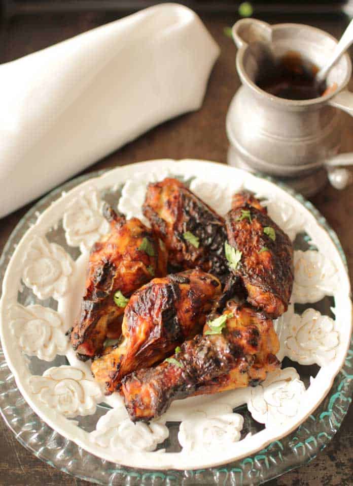 Five baked chicken wings on a plate next to a small metal container of BBQ sauce