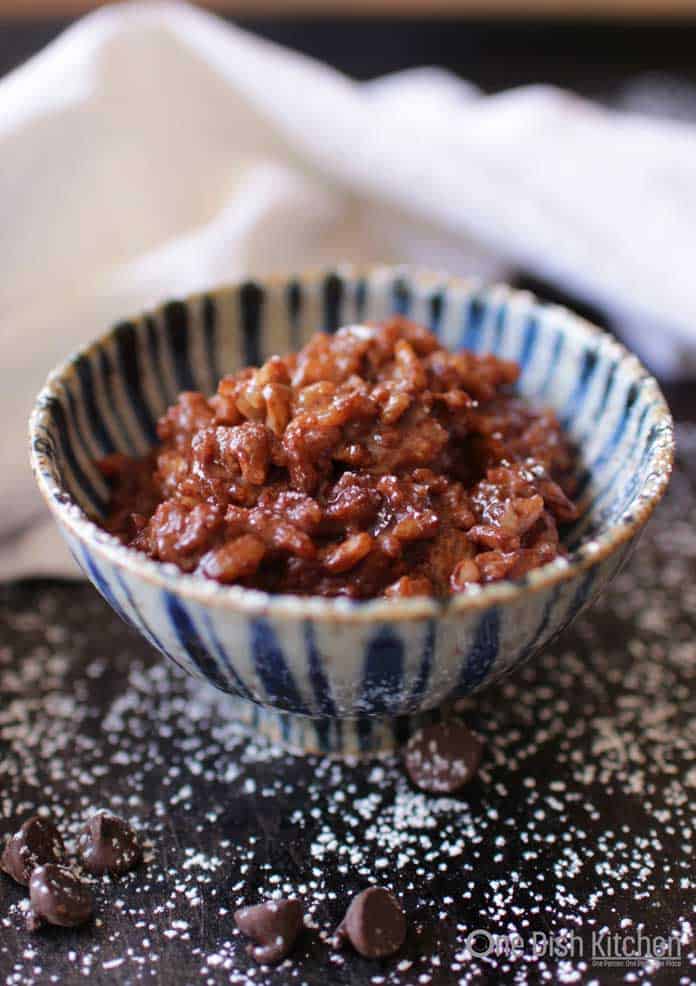 Chocolate rice pudding in a bowl on a dark surface with scattered chocolate chips and powdered sugar