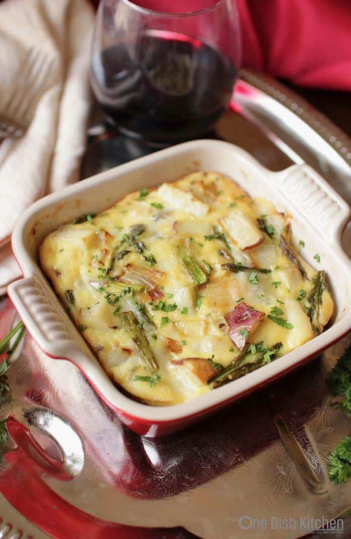 Potato and asparagus crustless quiche in a small baking dish on a metal tray with a glass of red wine