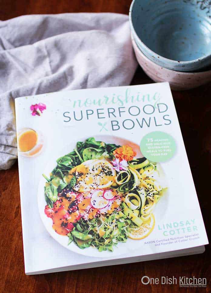 Nourishing Superfood Bowls Cookbook by Lindsay Cotter on a wooden table next to a stack of two bowls