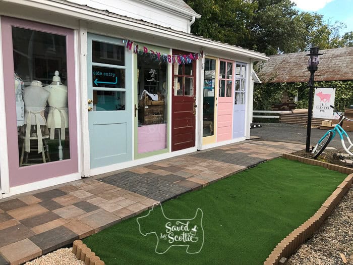side view of diy sunroom made from vintage doors with stone walkway and astroturf lawn in front with front end of a bicycle mailbox on the right